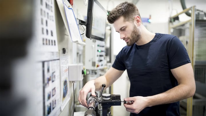 Young apprentice engineer operating mechanical fitting equipment in a workshop