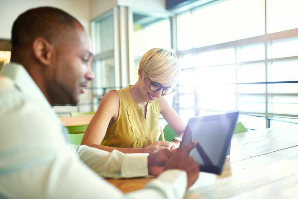 Two creative millenial small business owners working on social media strategy using a digital tablet while sitting at desk Two creative millenial small business owners working on social media strategy using a digital tablet while sitting at desk